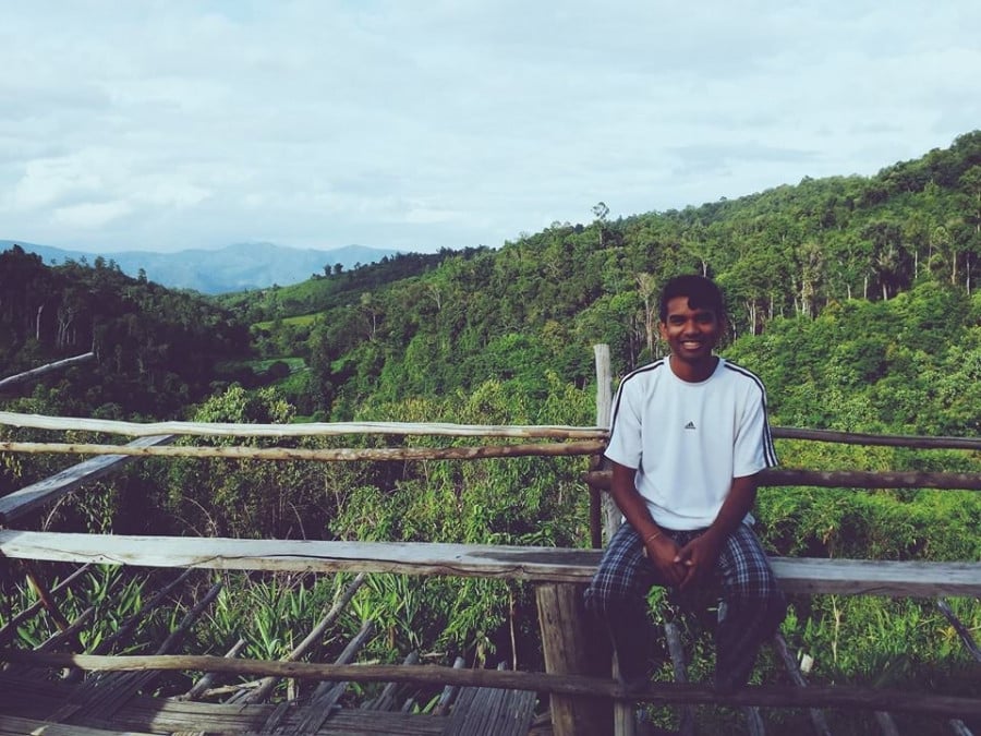 Eshan sitting down for a photo with lushe, dense, green forest in the background