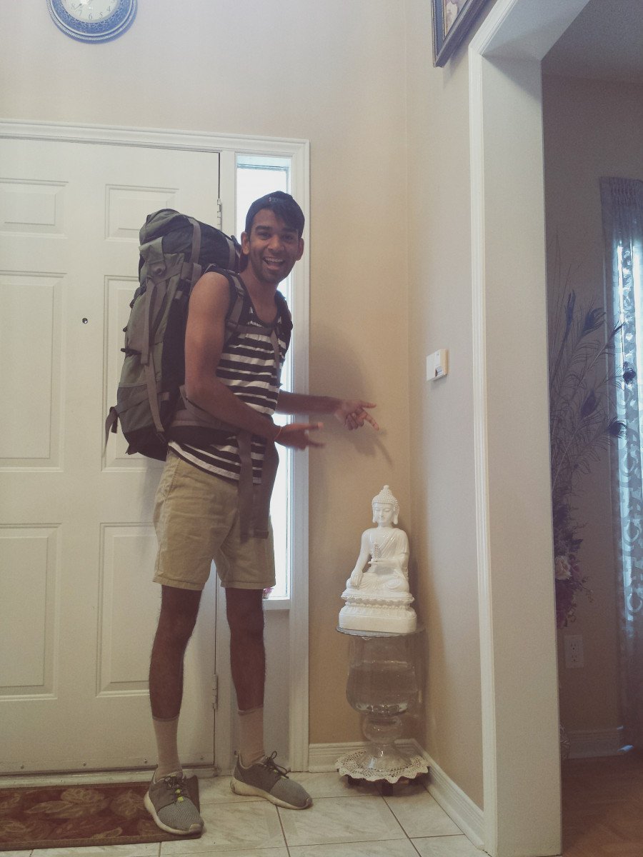 Eshan with his backpack on posing with a Thai statue at home