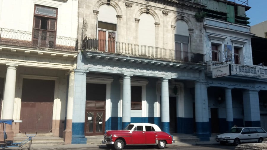 A Cuban streetfront with old buildings and a red classic car