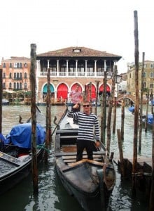 A man staning in a gondolier in a Venice channel, giving a thumbs up