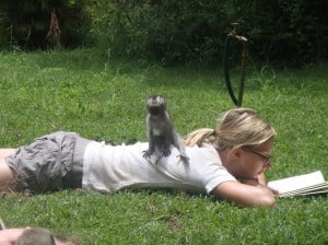 Jenny laying down reading a book with a baby monkey sitting on her back