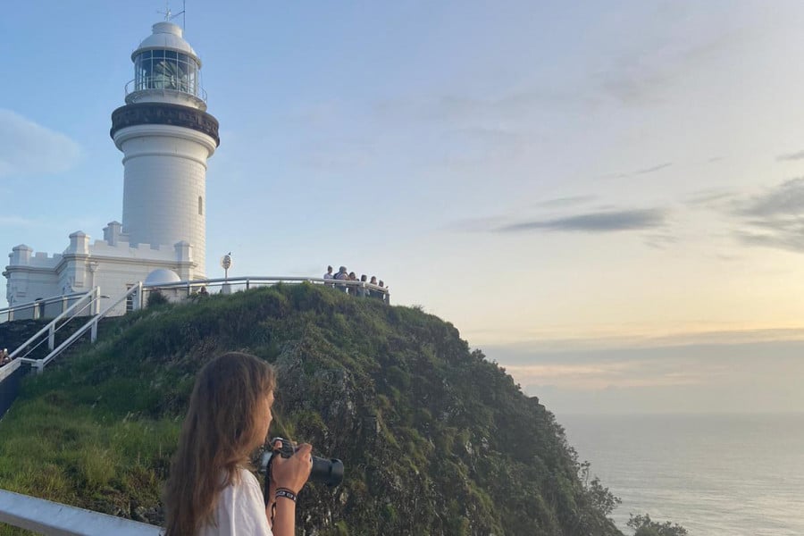 A travellers takes photos at a lighthouse on a cliff