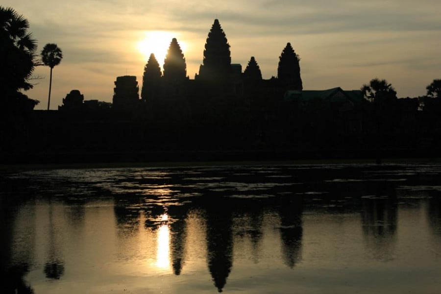 Angkor Wat temple reflecting over water below at sunset 