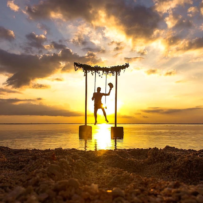 A person on a swing over water during sunset