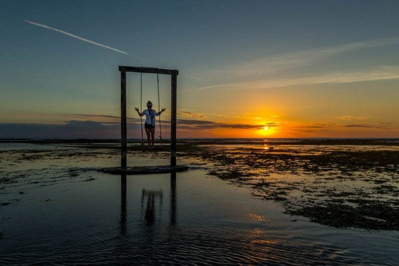 A traveller stands on a swing in the middle of water at sunset