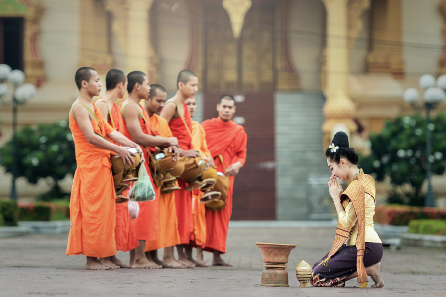 A lady kneeling in front of monks in orange robes