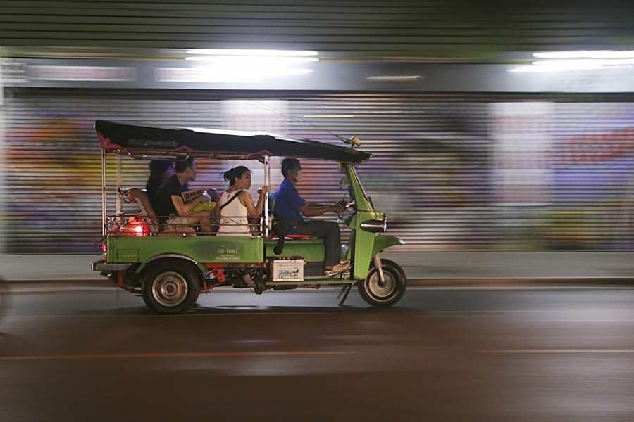 People riding down a street in a green Tuk Tuk