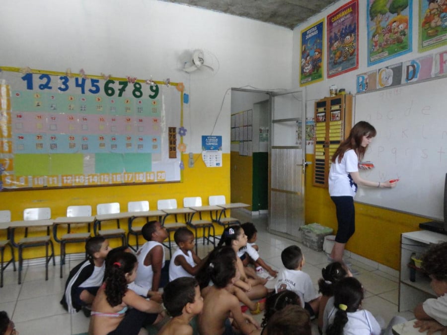 A volunteer teacher writes on a whiteboard in a classroom while schoolkids look on