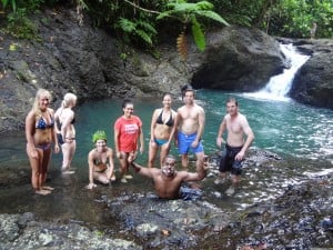 A group of people in a swimming hole by a waterfall