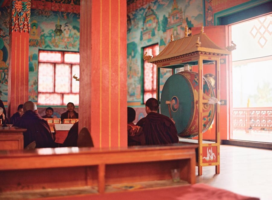 Buddhist monks in crimson robes sitting in a brightly coloured temple
