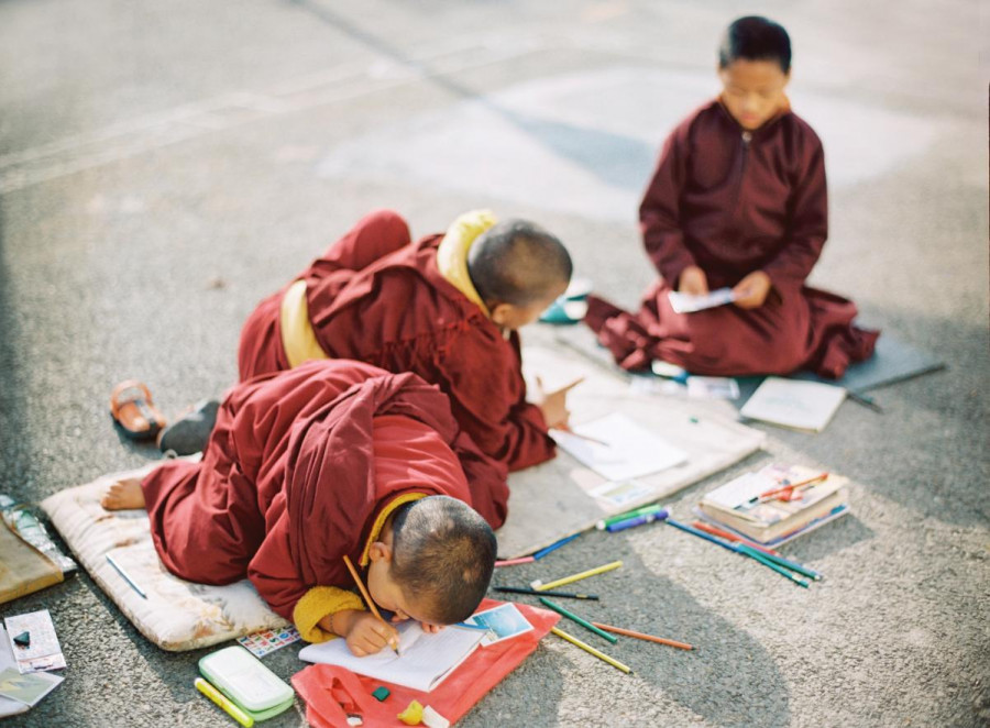 Three children in monk robes sit outside and draw on paper
