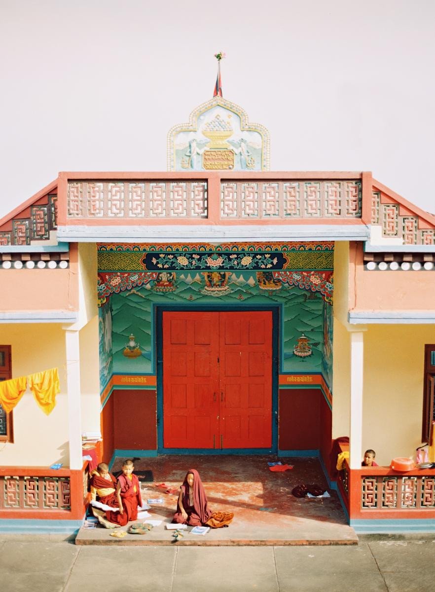 Brightly coloured entrance to a temple with children in robes sitting on the step