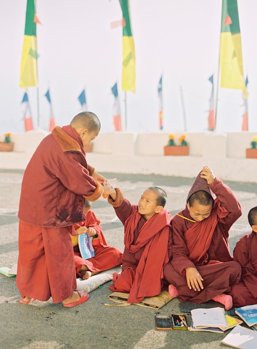Children in red Buddhist monk robes sit on the floor and draw in books