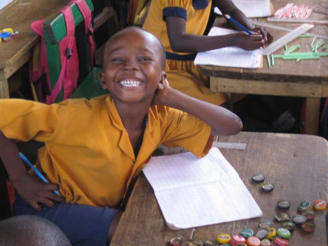 A Ghanian schoolkid smiling at a desk with their notebook