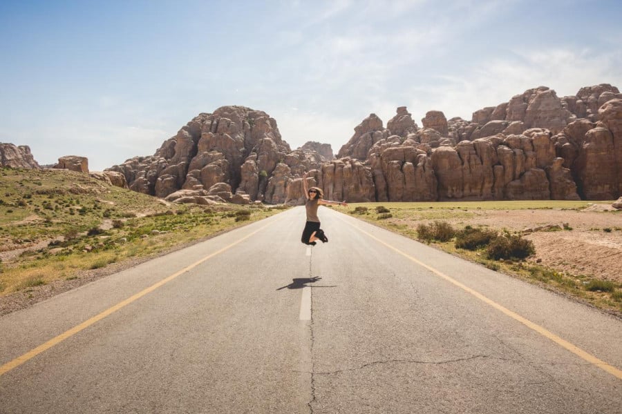 Person in the middle of a highway jumping into the air with rock formations in the background