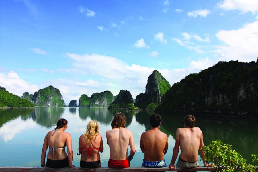 Travellers sit by the water in Halong Bay with islands in the background