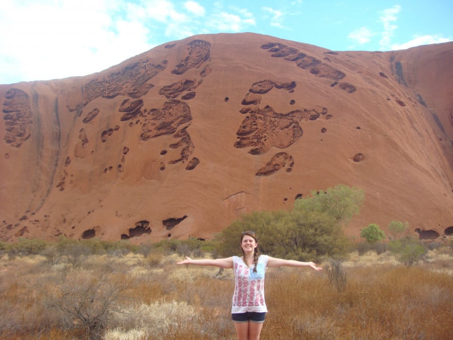 Madeleine standing with arms outstretched in front of Uluru
