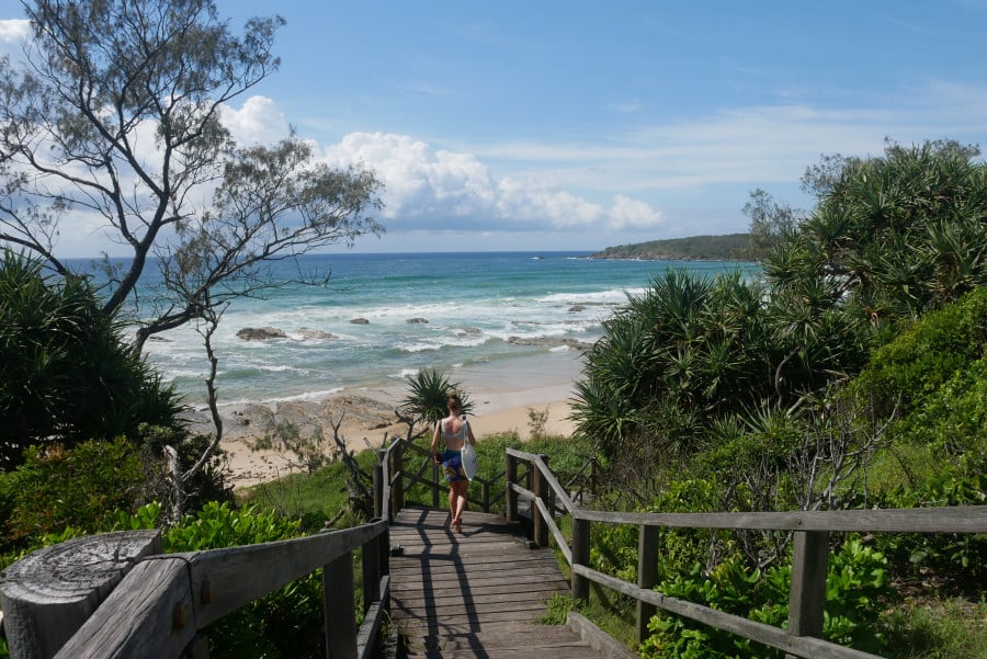 A traveller walks down a set of stairs to a secluded beach