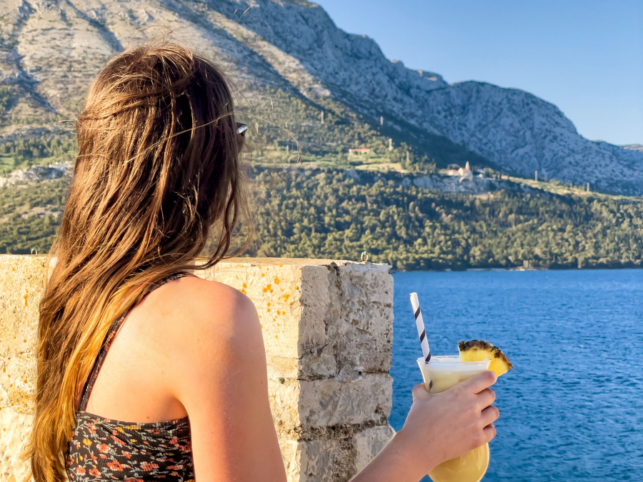 Traveller holding a cocktail overlooking the ocean and mountains in Croatia