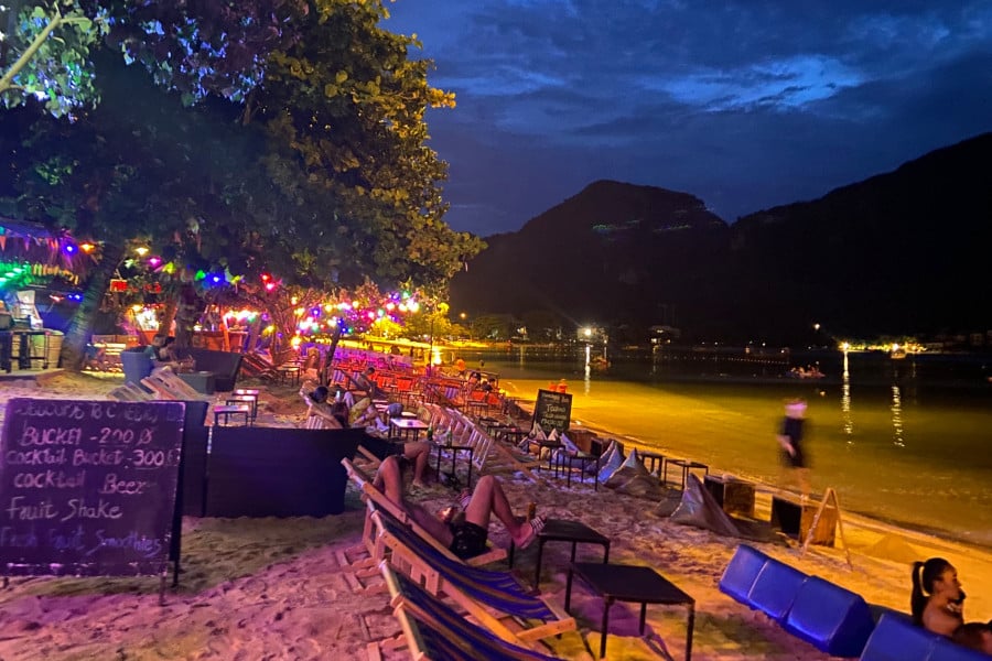 A colourfully lit beach bar with beach chairs on sand