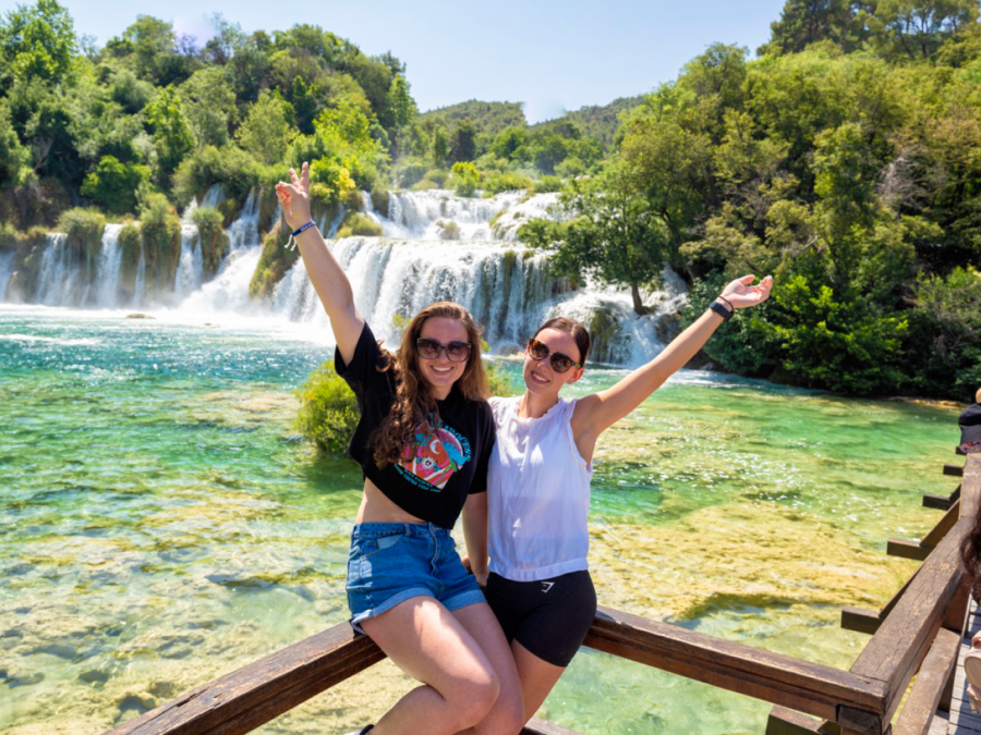 Travellers holding their hands in the air in front of a waterfall at Krka National Park