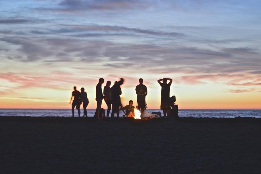 A group of people around a campfire on the beach at sunset