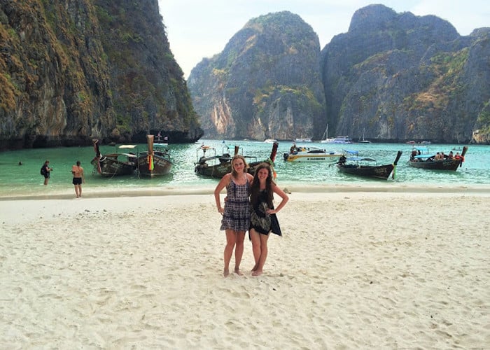 Two travellers standing on the beach in Maya Bay with blue water and rock formations in 