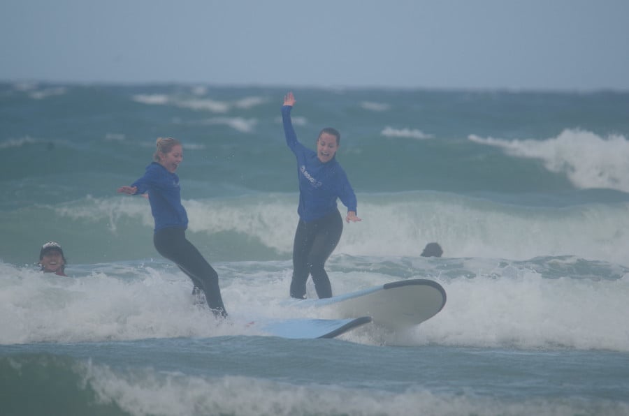 Two ladies riding a wave on surfboards