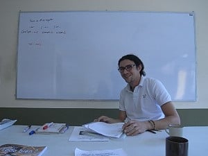 A language teacher sitting at a desk in front of a whiteboard
