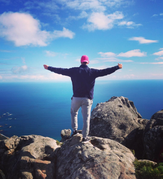 Man standing on a rock with arms outstretched overlooking the ocean