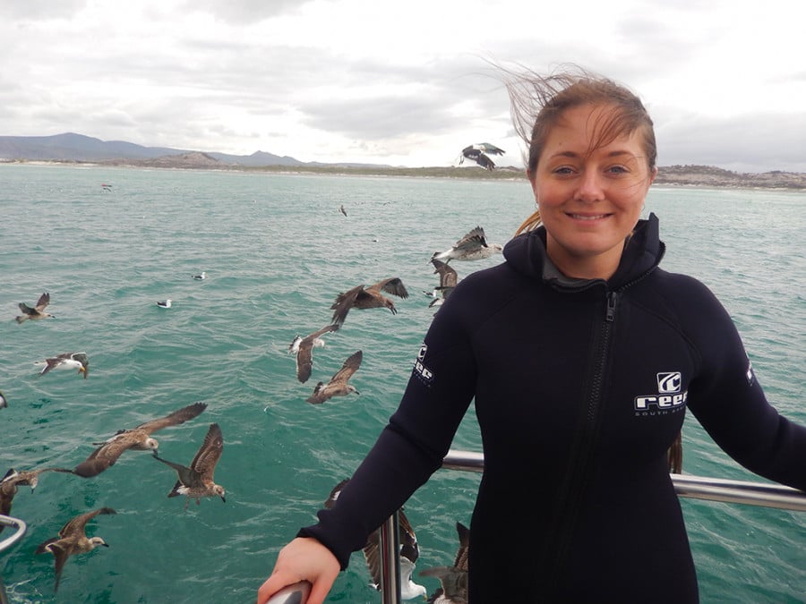 A lady in a wetsuit on a boat with seabirds and ocean in the background