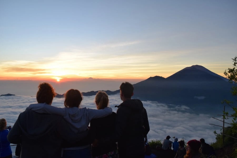 Travellers with their arms around wach other watching the sunset over a volcano